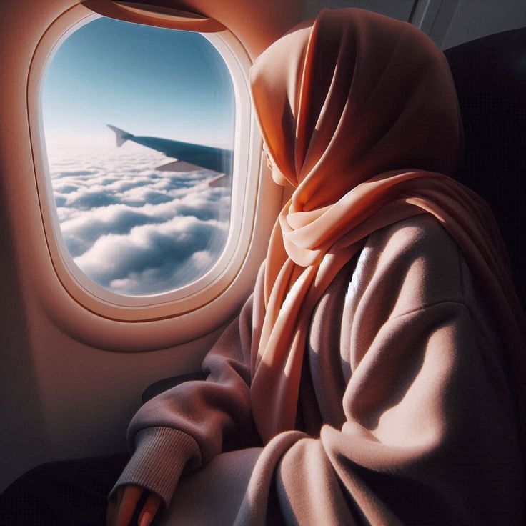 Woman in pink hijab looking out airplane window at clouds